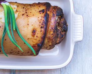 Baked meat roll with spices lies in a ceramic bowl on a table made of wood.