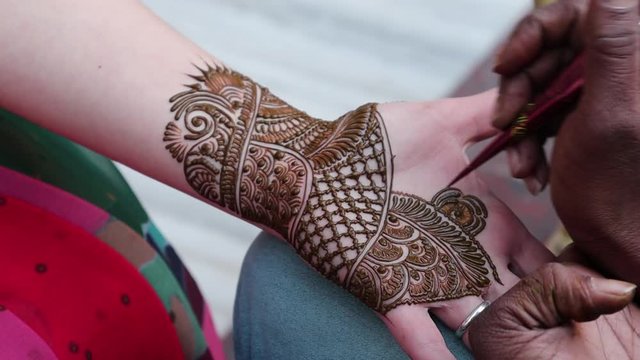 An artist is decoring the hand of a woman with traditional Indian temporary tattoo realized with henna paste during the Mehndi ceremony. Hindu wedding tradition and ritual. Agra, Uttar Pradesh, India.