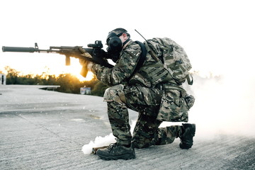 Army soldier in gas mask sitting in smoke with a rifle in his hands aiming at intruders. Military people keep order in the country during an emergency in the country caused by coronavirus