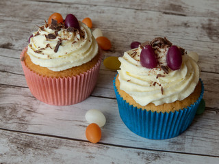 Colorful cupcakes decorated with creamy frosting jelly beans and chocolate sprinkles on wooden surface
