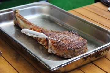 Fried Tomahawk beef steak in a metal vessel on a wooden table. Measuring the temperature of meat. Background image, copy space