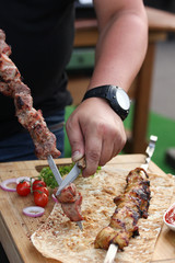 Meat and chicken skewers on pita bread with parsley, onion and cherry tomatoes on a wooden board with hands. Ketchup in a bowl. Picnic. Fried meat on the fire. Background image, copy space