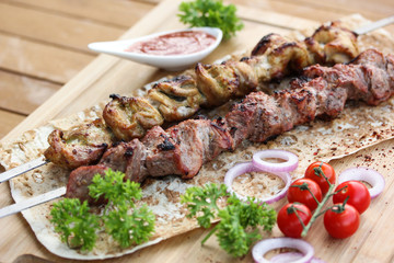 Meat and chicken skewers on pita bread with parsley, onion and cherry tomatoes on a wooden table. Ketchup in a bowl. Picnic. Fried meat on the fire. Background image, copy space