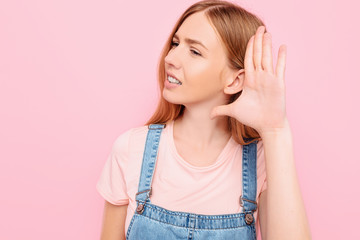 Focused girl listening with hand to ear isolated on pink background