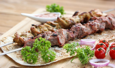 Meat and chicken skewers on pita bread with parsley, onion and cherry tomatoes on a wooden table. Ketchup in a bowl. Picnic. Fried meat on the fire. Background image, copy space