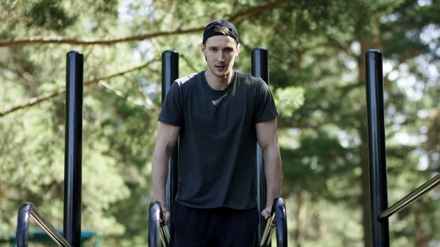 Adult caucasian athlete is pulling up his legs on bars ath the gym at the park, frontal shot