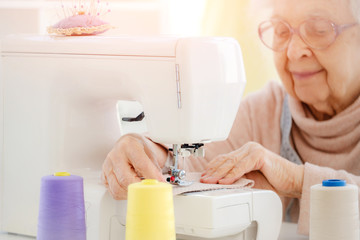 Lovely aged woman sewing at workshop