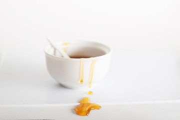 Drips of sweet honey on a white bowl on a white table with soft light.