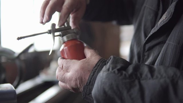 Old man closes an oil spray gun and proceeds to lubricate a machine with it