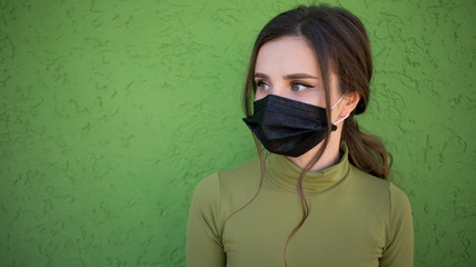Beautiful girl on the green background with flu medical face mask. Protected and saved from respiratory problems.