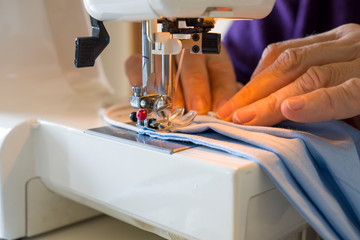 Homemade antivirus mask. Sewing machine, hands preparing a blue mask to protect themselves from...
