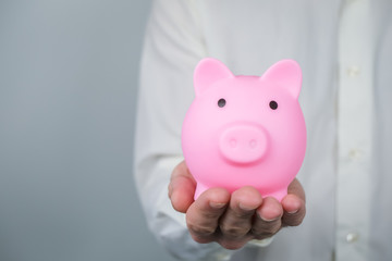Pink piggy bank in mans hands. Concept of saving and earning money, investments. Copy space.