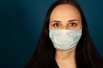 Portrait of young woman in medical mask on her face on blue background. Adult female protecting yourself from diseases. Concept of threat of coronavirus epidemic infection.