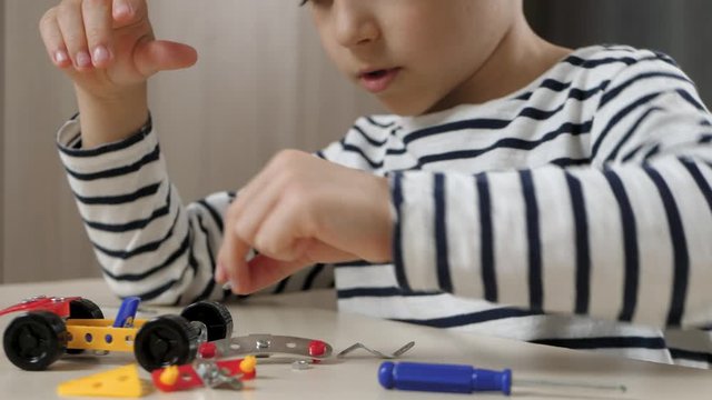 A child designs a model of a small toy car. A happy child plays with a constructor while sitting at a table. The camera moves from the child's hands to the child's face.