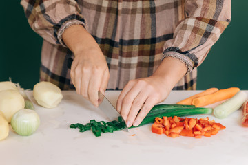 Woman cuts fresh green onion at her kitchen on white marble, to prepare her food.