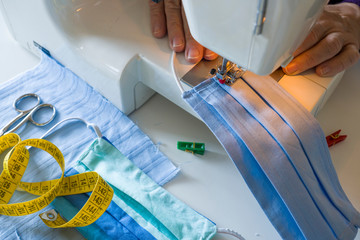 Homemade antivirus mask. Sewing machine, hands preparing a blue mask to protect from Covid-19 viral...
