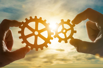 Silhouettes of hands connect gears to a puzzle on sunset background. Business concept idea. Association, cooperation, teamwork, partnership. Close-up