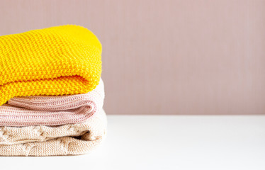 A stack of warm knitted things on a white table. Cozy clothes. Household concept.