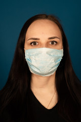 Portrait of young woman in medical mask on her face on blue background. Adult female protecting yourself from diseases. Concept of threat of coronavirus epidemic infection.