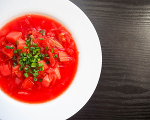 White round plate with soup of national cuisine borscht with sliced green onion rings on the background of a dark wooden table