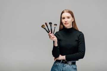 attractive makeup artist holding makeup brush set isolated on grey