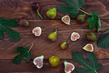 Ripe figs whole and cut in half with green leaves on a brown wooden background top view