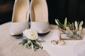 Accessories of the bride. Wedding rings lie next to women's high heel shoes and groom's boutonniere