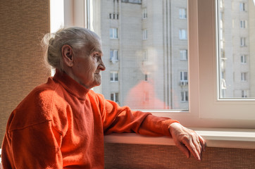 An elderly woman looks out the window on a sunny day