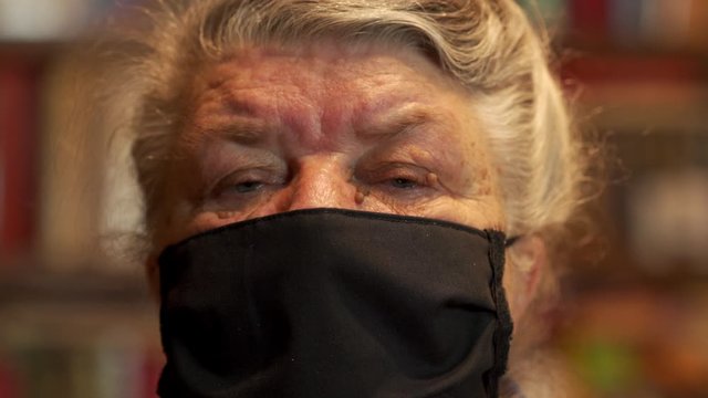 Senior person in protective sterile medical mask on her face looking at camera close-up, corona virus pandemic, washable reusable black dustproof mouth face mask.