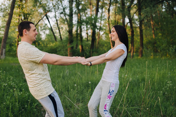 Loving guy and girl are spinning, holding hands, in nature, in tracksuits for a walk. Love story newlyweds. Fun photo, concept.