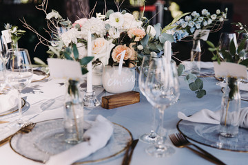 Wedding decor in blue and gray. Banquet tables with tablecloths are decorated with compositions of flowers, on the tables are plates, glasses and candles