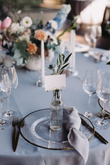 Wedding decor in blue and gray. Banquet tables with tablecloths are decorated with compositions of flowers, on the tables are plates, glasses and candles