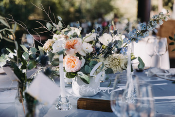 Wedding decor in blue and gray. Banquet tables with tablecloths are decorated with compositions of flowers, on the tables are plates, glasses and candles