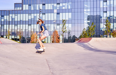 Young woman in short skirt skating on longboard outdoor in a skate park.
