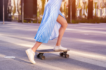 Skater woman in dress is training on longboard, doing a trick outdoor in a public park. Close up view on shoes.