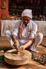 Fototapeta na wymiar Indian potter at work: throwing the potter's wheel and shaping ceramic vessel and clay ware: pot, jar in pottery workshop. Experienced master. Handwork craft from Shilpagram, Udaipur, Rajasthan, India