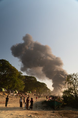 smoke from a burning ship near an asian river in a poor town