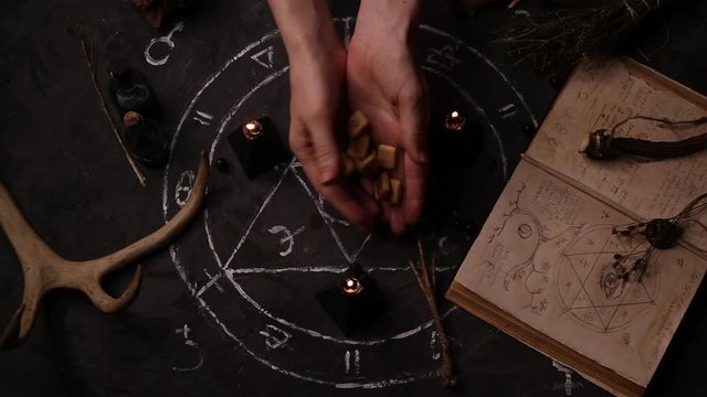 Woman witch divines on wooden runes. Black magic candles burn against the background of the magical attributes of black magic. Halloween concept