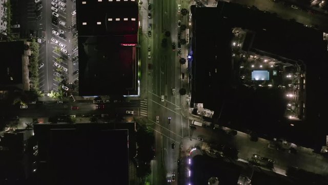 AERIAL: Overhead View on Wilshire Boulevard Street in Hollywood Los Angeles at Night with Glowing Streets and City Car Traffic Lights 
