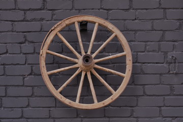 A wooden wheel from a cart against a black brick wall.