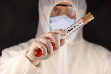 The doctor in a protective suit and mask holding a glass tube with a positive blood test result for...