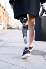 Low section of woman with leg prosthesis walking in the city