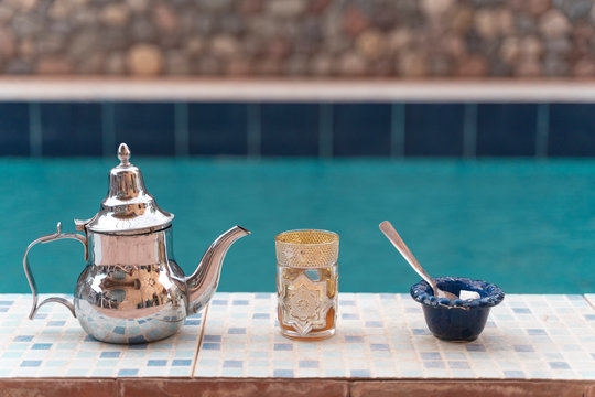 Silver tea pot, tea glass and sugar bowl on poolside