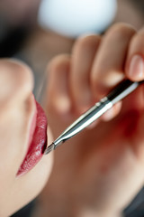 cropped view of makeup artist applying lipstick on woman