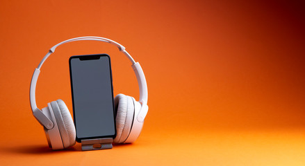 White headphones with smartphone mockup, isolate on orange, music online concept.