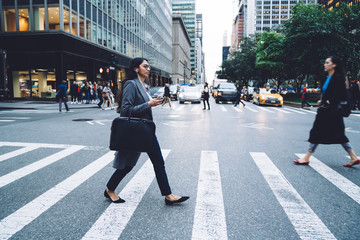Modern young female listening to music while crossing street