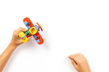 Kid hands play with toy airplane on white background. Top view