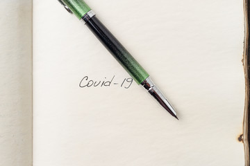 Covid-19 coronavirus inscription on a blank empty sheet of paper in a notebook. Nearby lies a pen. A lot of space for inscriptions and copyspace. Blank for inscriptions. Template for article or cover.
