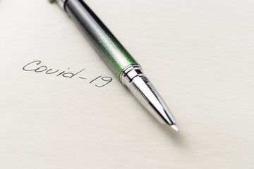 Covid-19 coronavirus inscription on a blank empty sheet of paper in a notebook. Nearby lies a pen. A lot of space for inscriptions and copyspace. Blank for inscriptions. Template for article or cover.