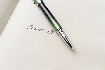 Covid-19 coronavirus inscription on a blank empty sheet of paper in a notebook. Nearby lies a pen. A lot of space for inscriptions and copyspace. Blank for inscriptions. Template for article or cover.